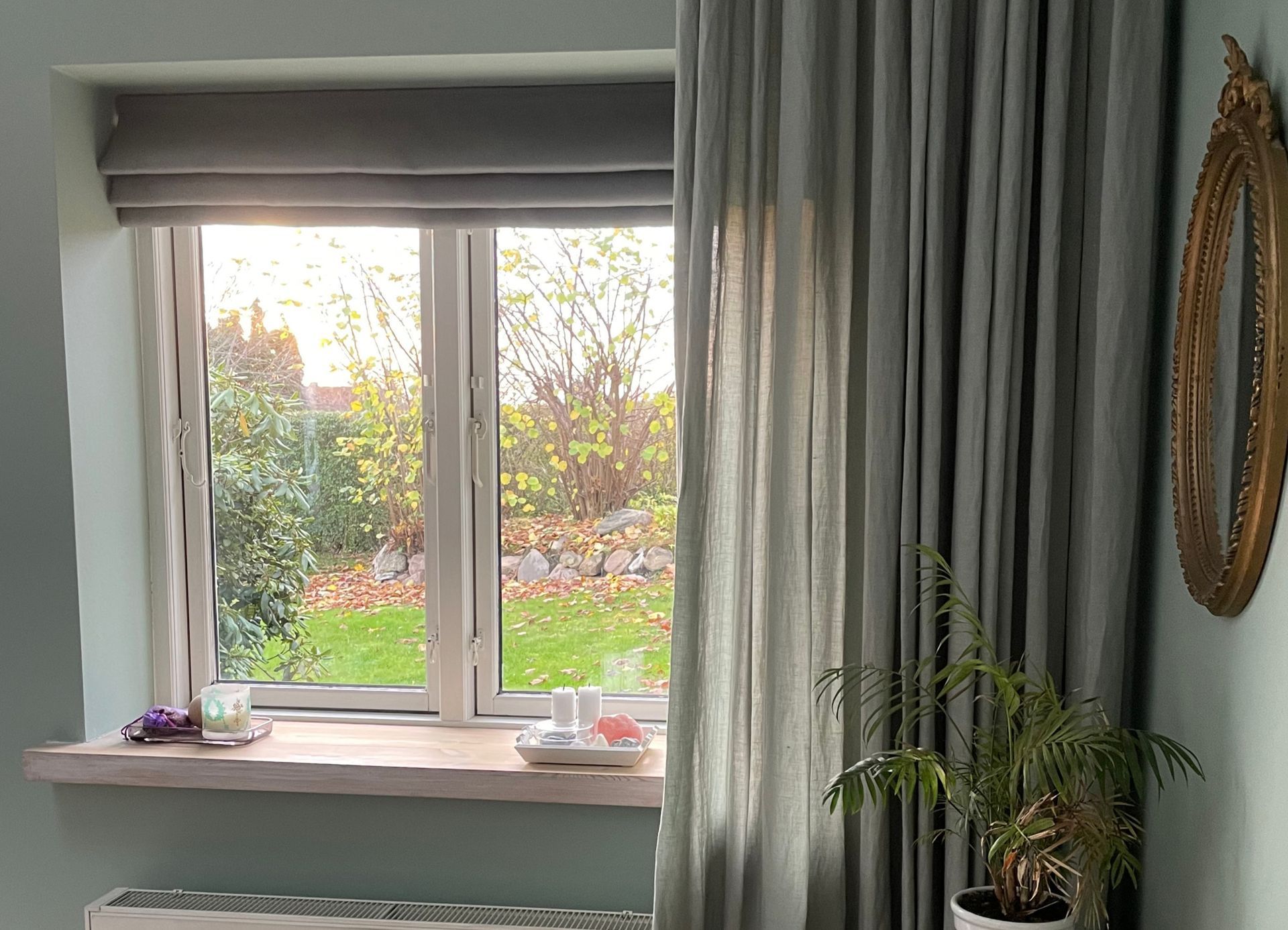 Vindue med tynde hvide gardiner og lange, brune gardiner mod en hvid væg og gulv.