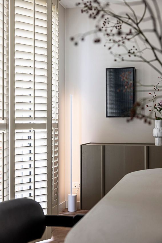 Åben hvid dør og vinduer med skodder, med udsigt over en grøn græsplæne. En træstol står ved vinduet.