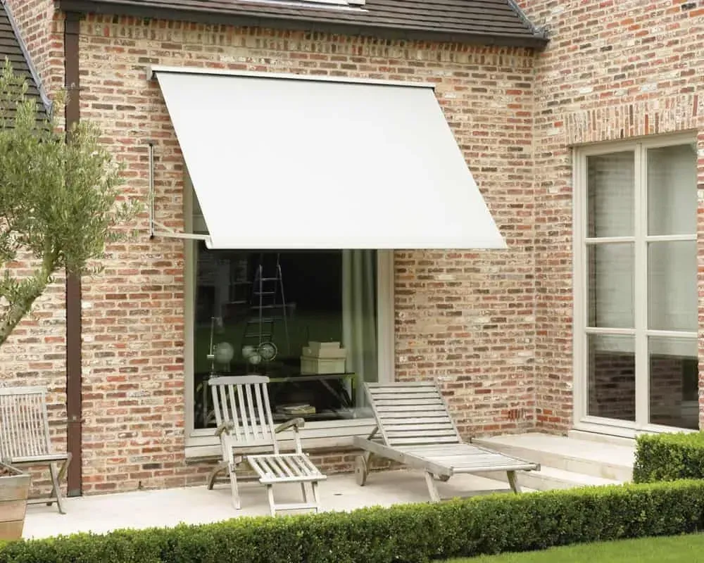 Hvid markise over et vindue på en murstensbygning med udendørs siddepladser.