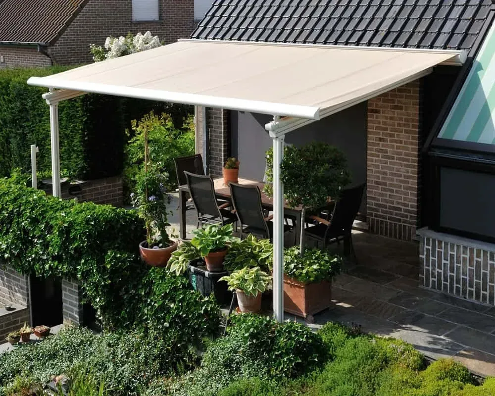 Beige markise over en terrasse med spisebord og stole, omgivet af potteplanter og grønne områder.