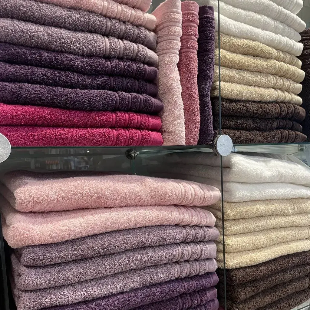 Hylder stablet med badehåndklæder i forskellige farvede, herunder lyserøde, lilla og brune.