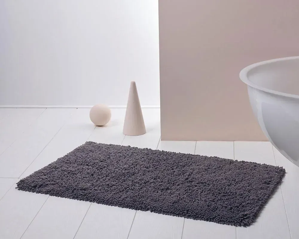Gråt badetæppe på hvidt gulv med en bold, en kegle og et badekar.