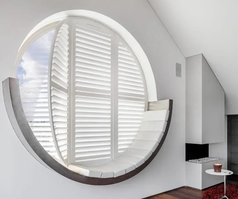 Åben hvid dør og vinduer med skodder, med udsigt over en grøn græsplæne. En træstol står ved vinduet.