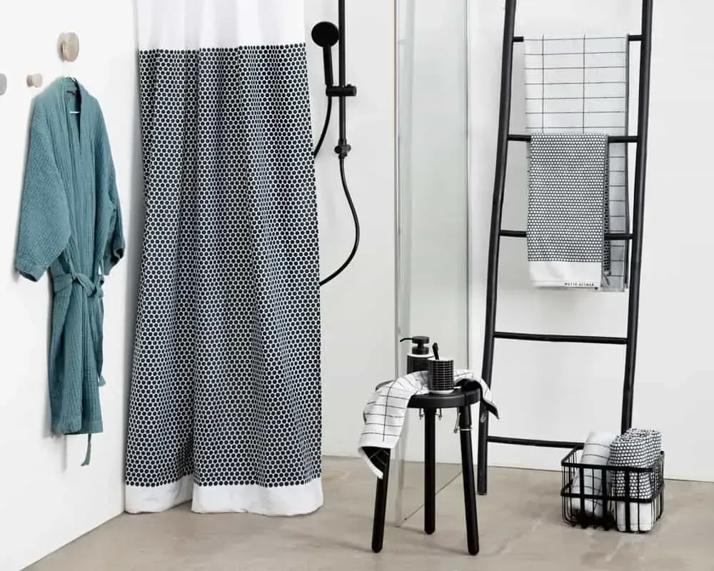 Badeværelse med mønstret bruseforhæng, badekåbe, sort stige med håndklæder og skammel.