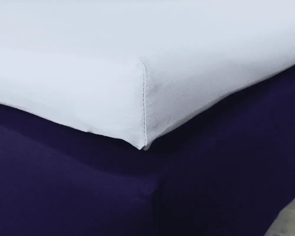 Hvidt lagen oven på et mørkelilla lagen.