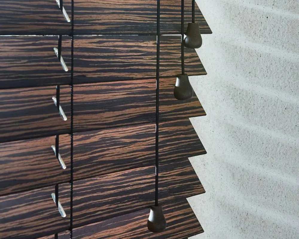 Træpersienner, der kaster skygger på en tekstureret, råhvid væg.