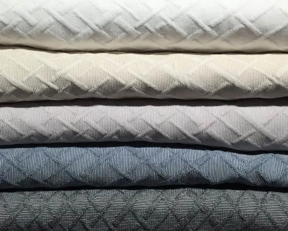 Bunke af stoffer i forskellige nuancer af hvid, grå og blå med et tekstureret diamantmønster.