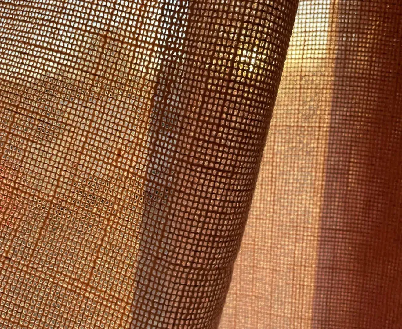 Nærbillede af brunt, tekstureret stof, oplyst af sollys, der kaster skygger.