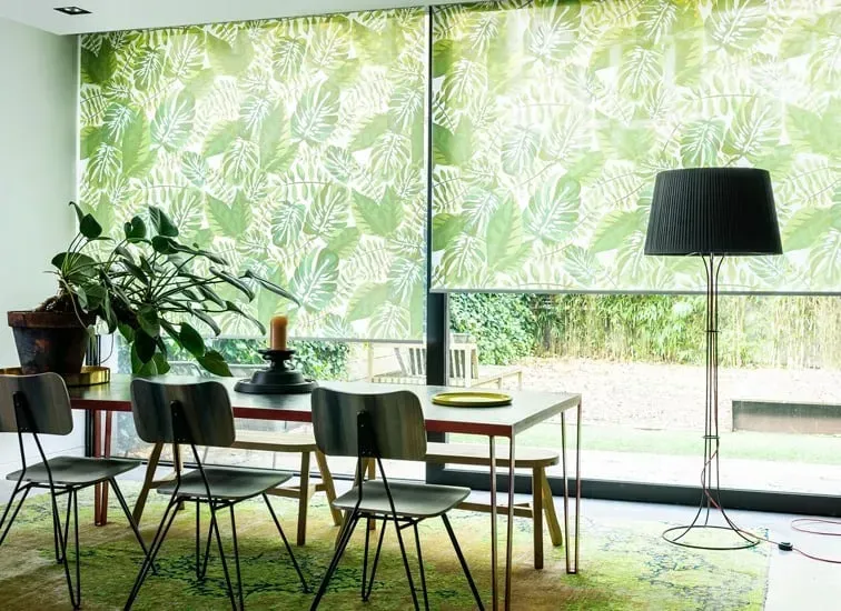 Spisestue med bord, stole, løvfældende persienner og en høj lampe.