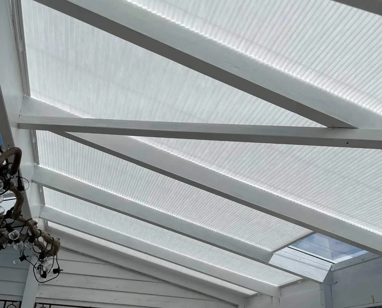 Hvidt indrammet pergolatag med gennemskinnelige bølgepappaneler, vinklet over et lyst rum.