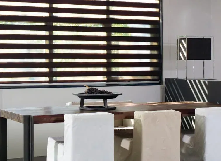 Spisestue med mørkt træbord, hvide stole og stribede persienner.