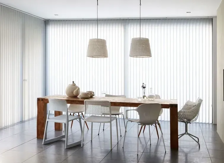 Spisestue med træbord, forskellige hvide stole og hængende pendellamper; lodrette persienner.