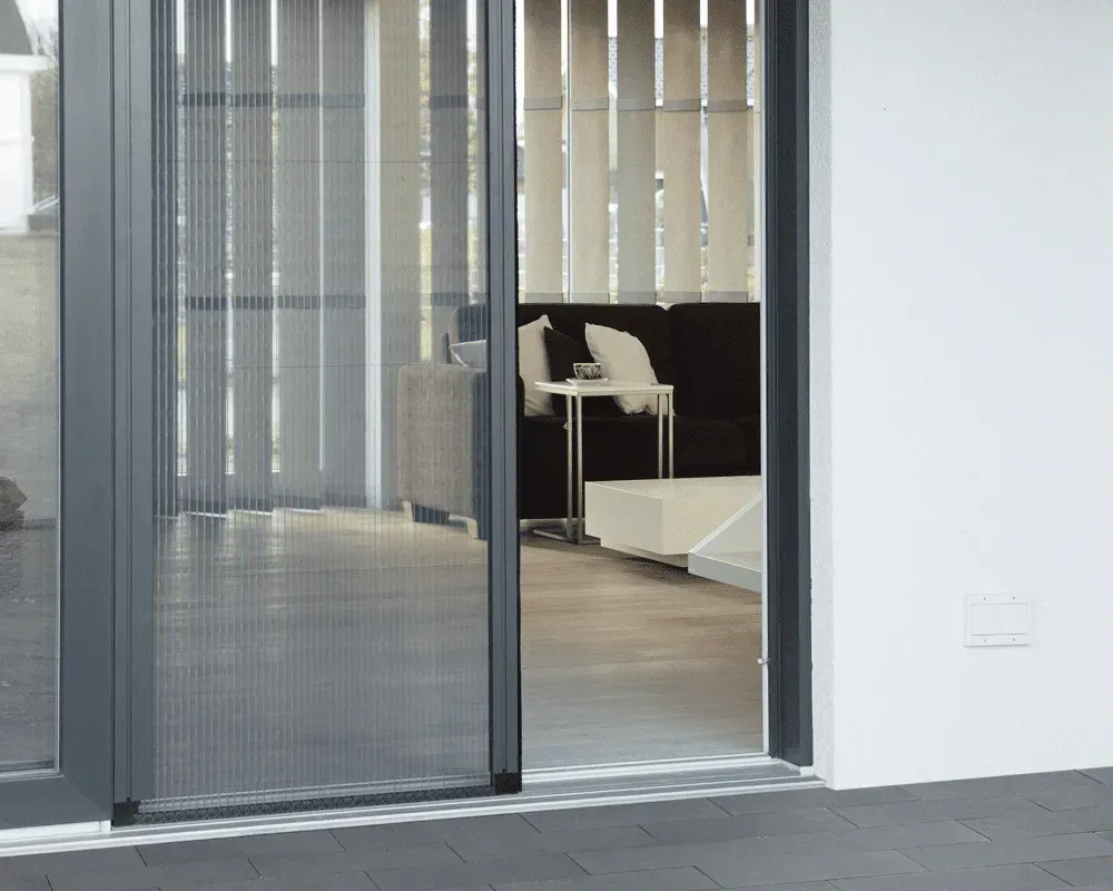 Skydedør med skærm, grå ramme, åben; fører til indendørs brug med møbler og persienner.