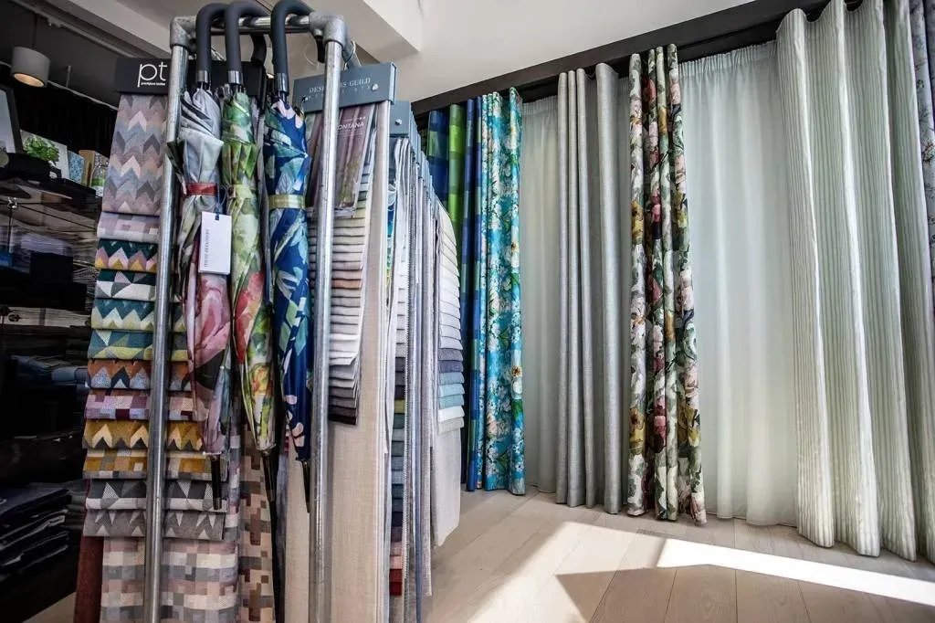 Gardinstofprøver udstillet i en butik, med farverige mønstre og ensfarvede lyse gardiner.