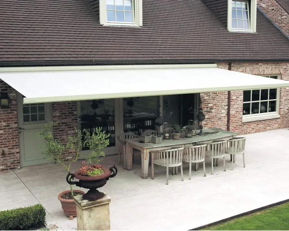 Udtrækkelig markise, der skygger for en terrasse med spisebord og stole, placeret op ad et murstenshus.
