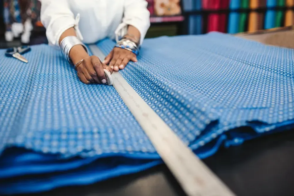Person bruger en lineal til at måle og markere blåt mønstret stof på et bord.
