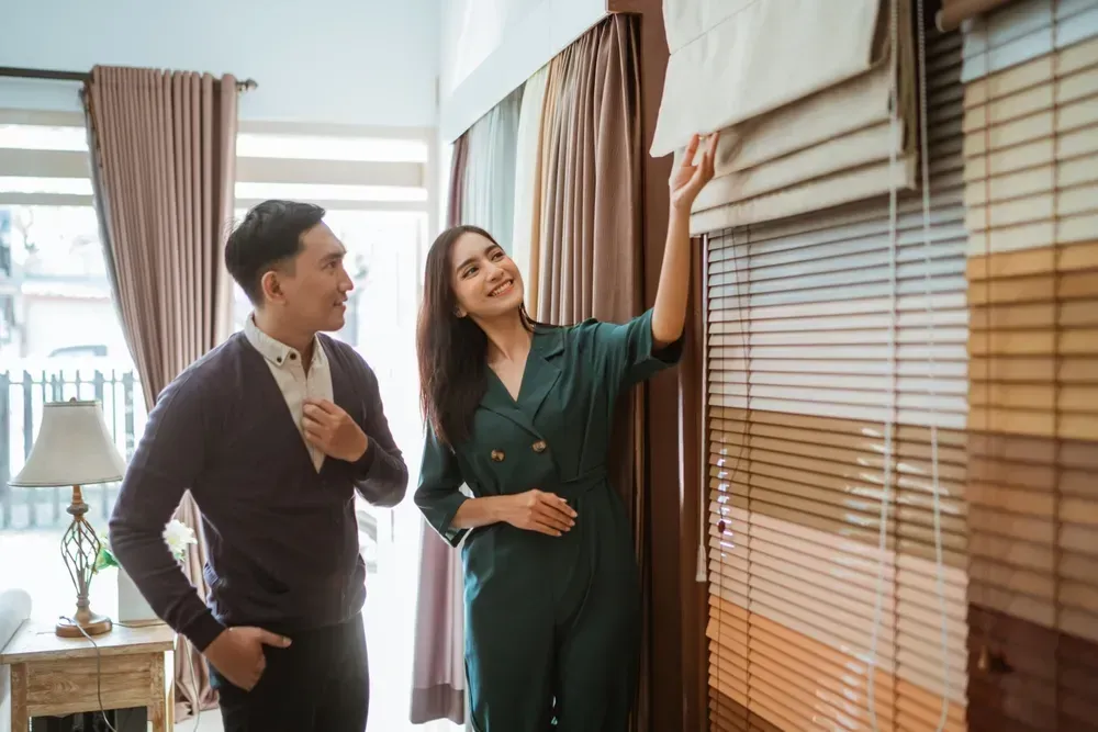 Par vælger persienner i et udstillingslokale, kvinde peger, mand smiler, forskellige farveprøver.