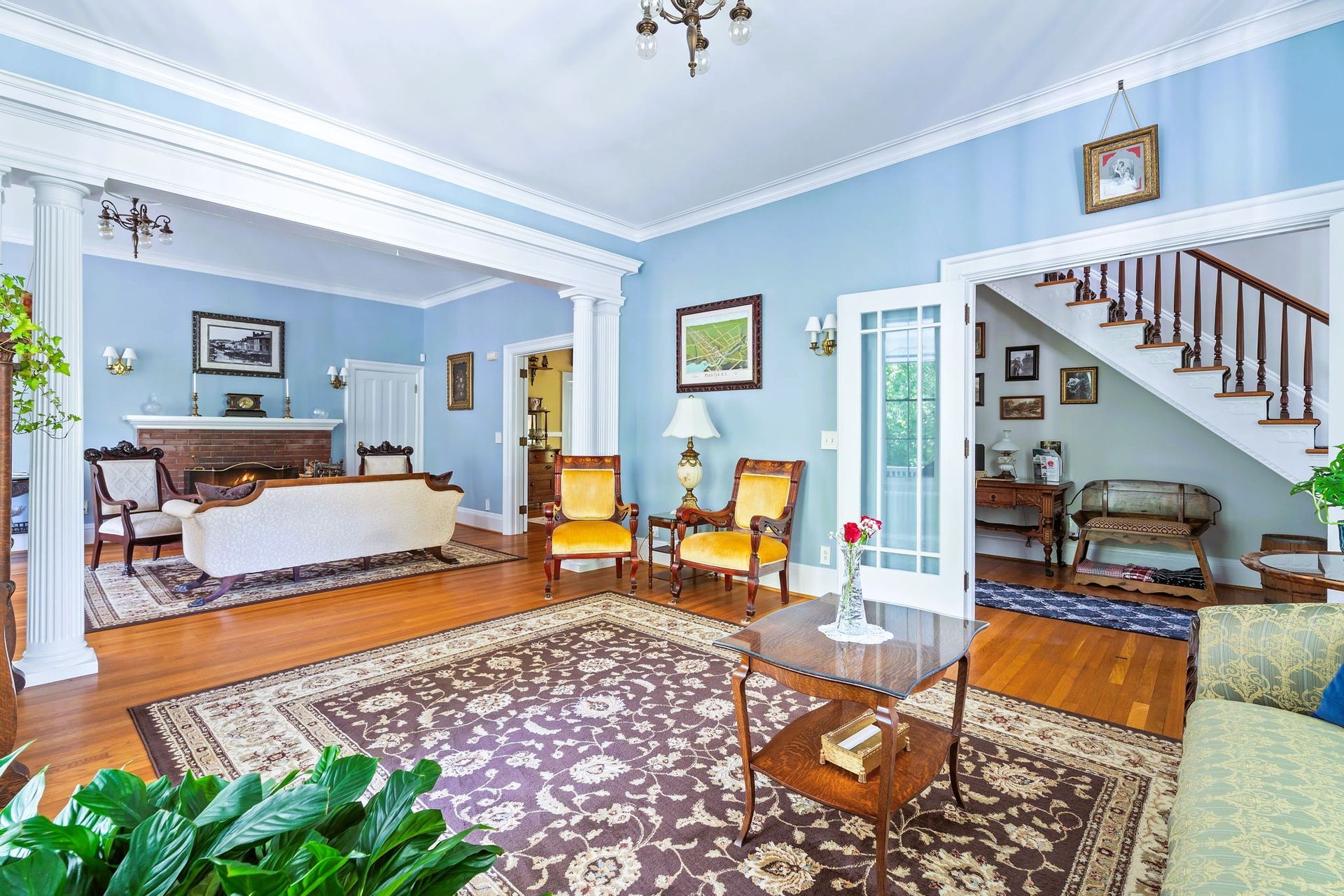 Bright living room with blue walls, patterned rugs, sofa, chairs, and a staircase leading upstairs