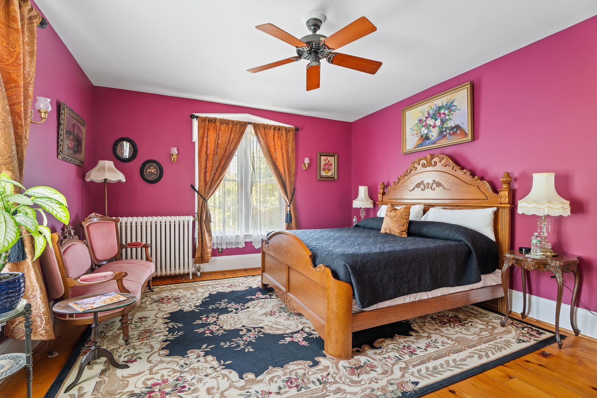 Bright pink bedroom with a wooden bed, patterned rug, ceiling fan, and French doors with curtains