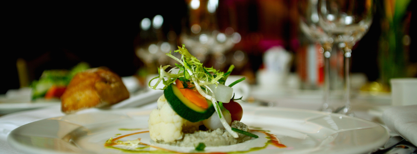 Plated gourmet dish with greens and vegetables on a white tablecloth at a formal dinner