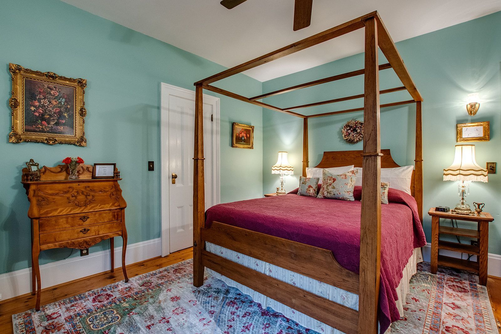 Bright bedroom with a four-poster bed, teal walls, antique dresser, and floral rug