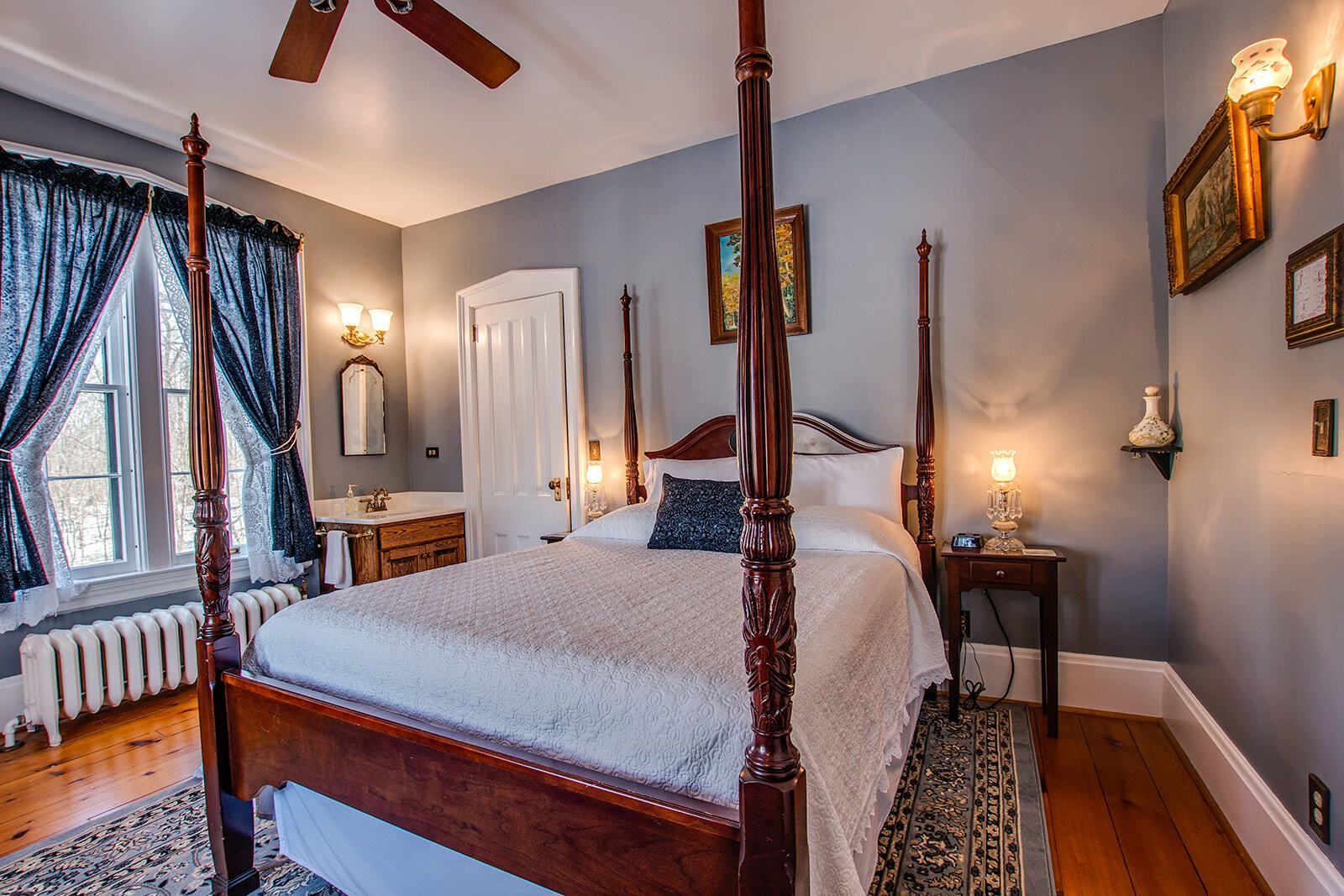Bedroom with four-poster bed, gray walls, hardwood floors, and warm bedside lamps