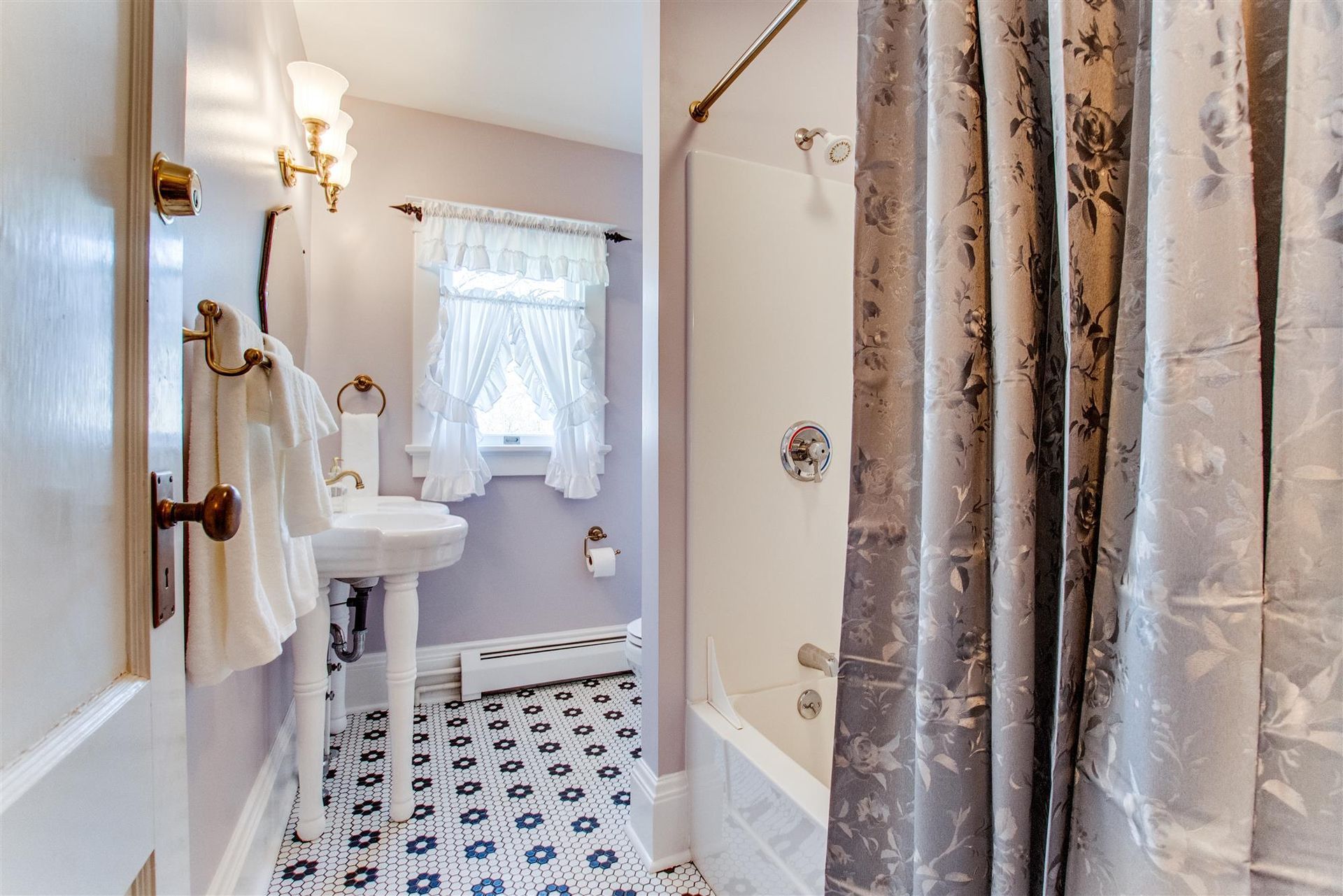 Narrow bathroom with white sink, floral curtains, and black-and-white patterned tile floor.
