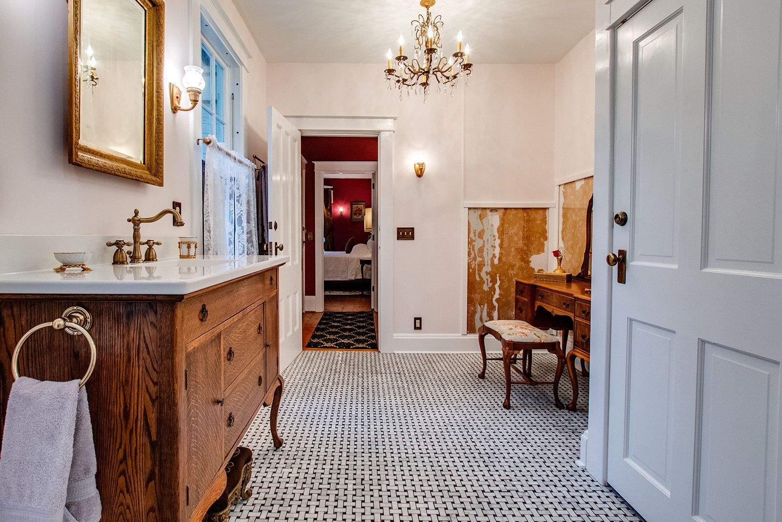 Elegant hallway with patterned tile floor, chandelier, wood vanity, chair, and open door to a red room