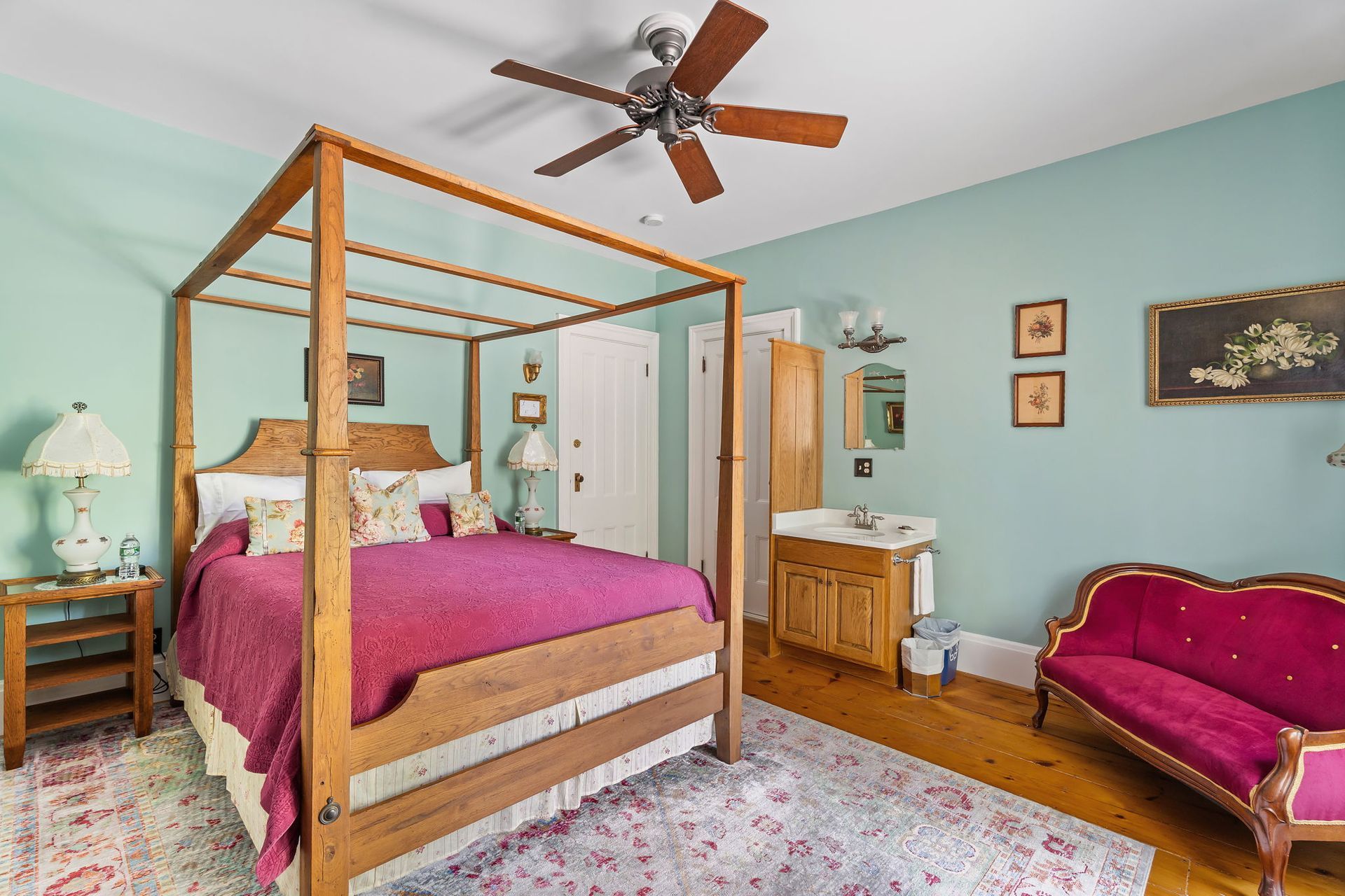 Bedroom with four-poster bed, pink bench, light blue walls, wood furniture, and ceiling fan.