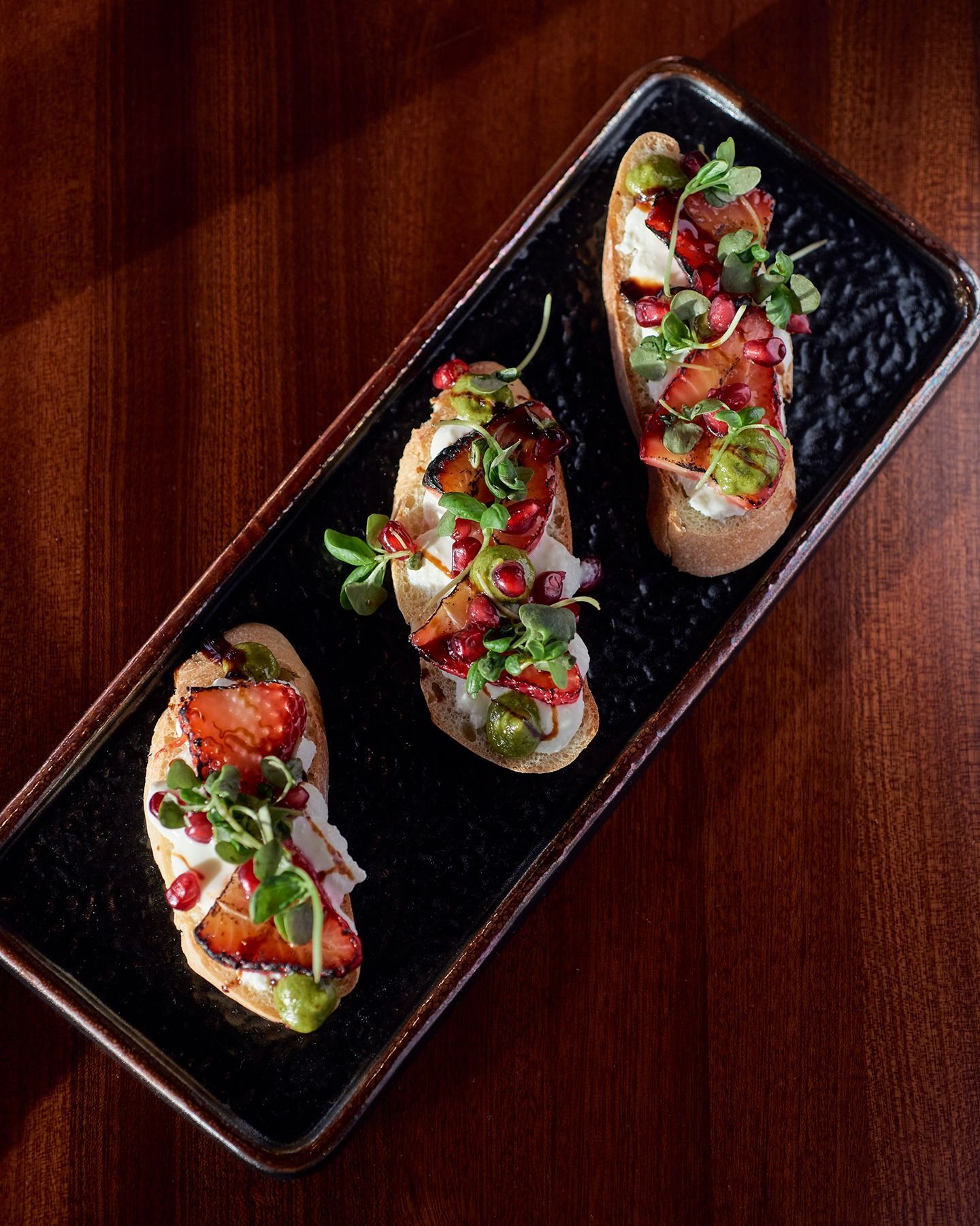 Three savory appetizers on a black platter, topped with herbs, diced vegetables, and red sauce