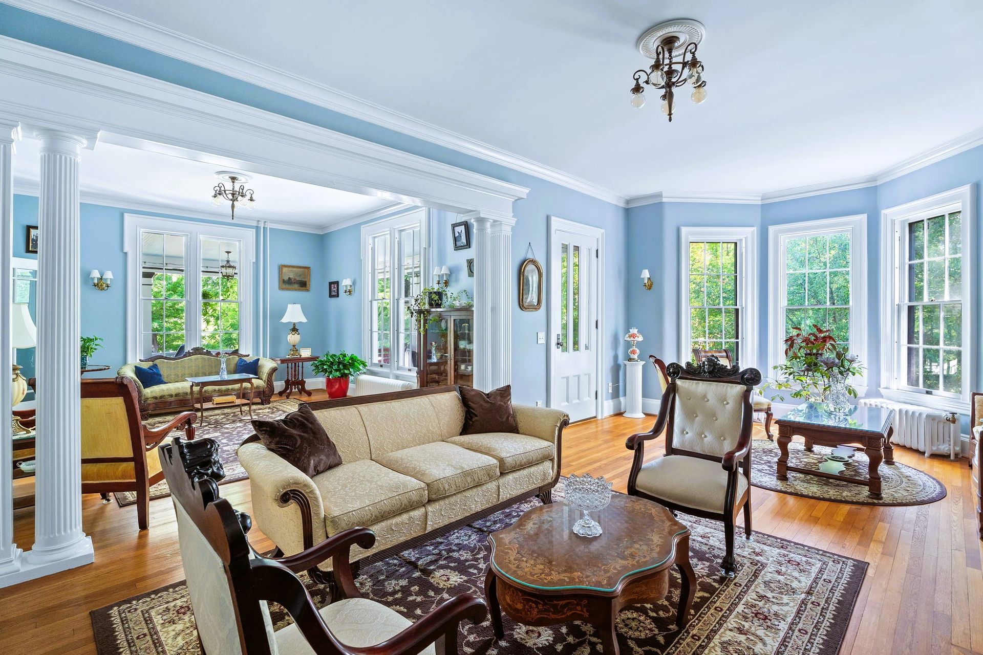 Elegant blue living room with cream sofas, carved wood chairs, and large windows with garden views