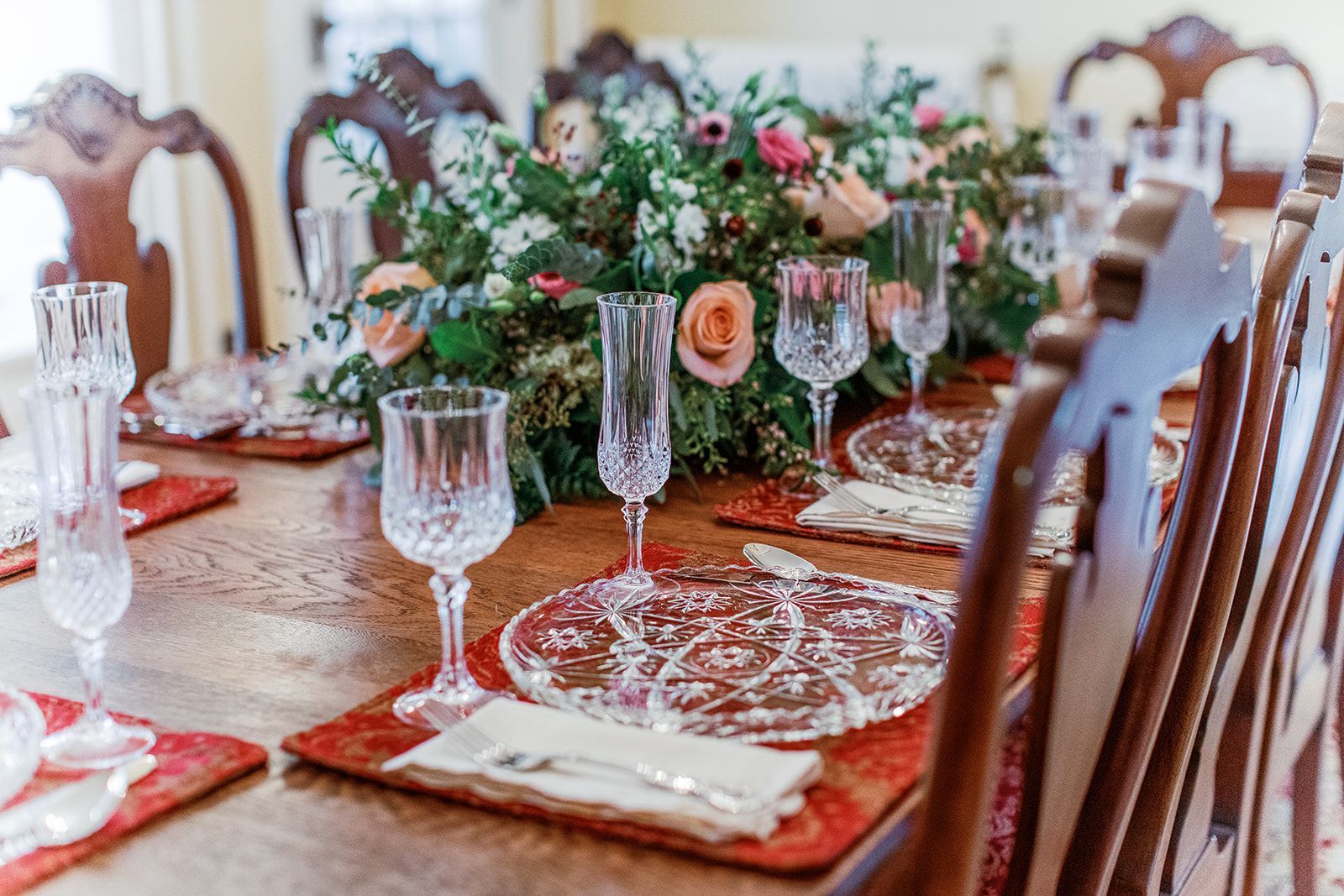 Elegant dining table set with crystal glasses, floral centerpiece, and red placemats