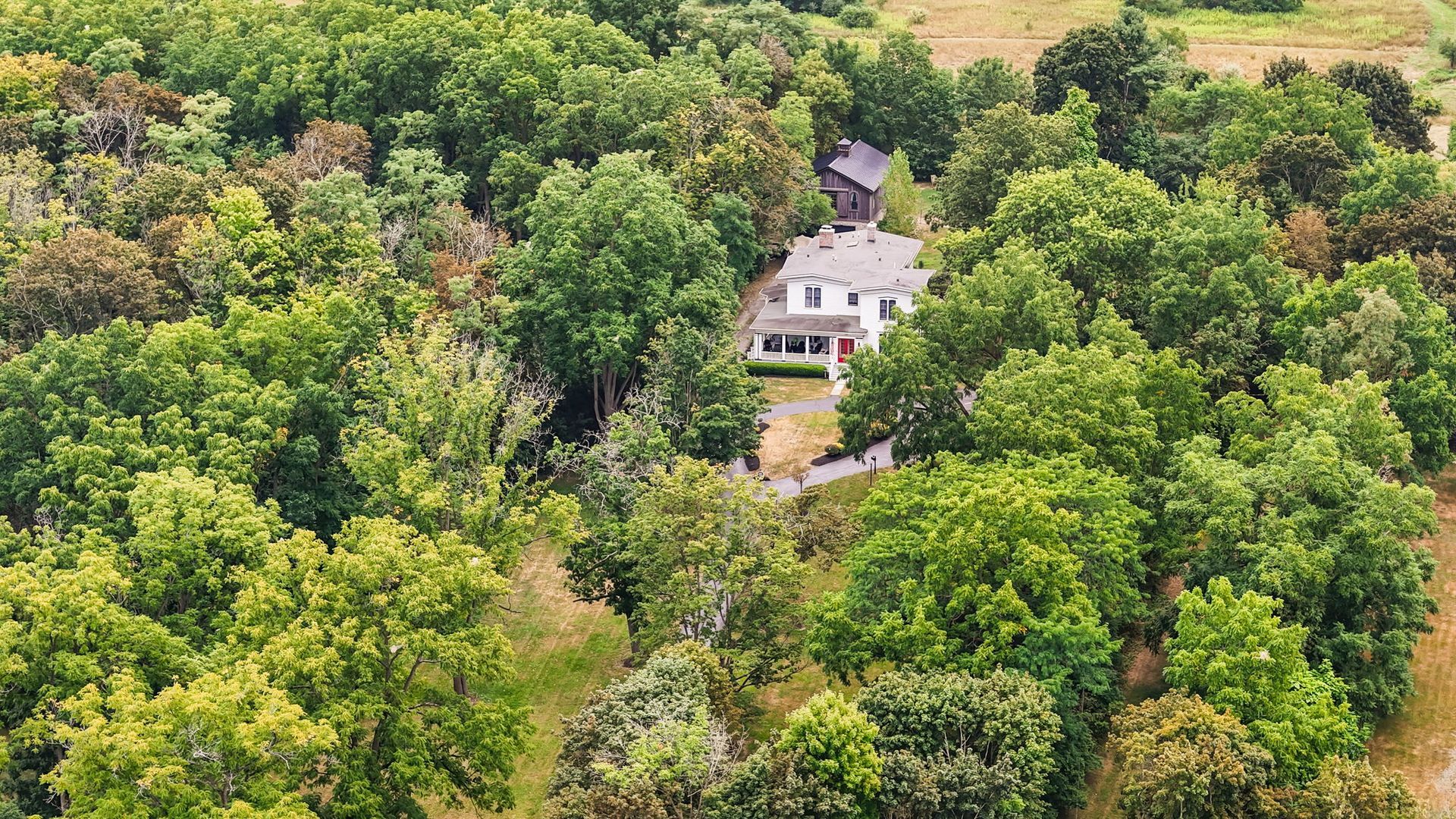A white house with a red roof nestled among dense green trees in a rural landscape.