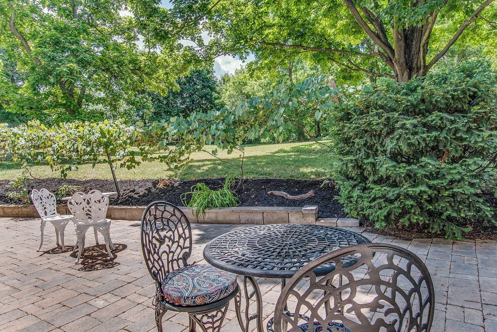 Patio with metal table and chairs overlooking a lush green garden and trees