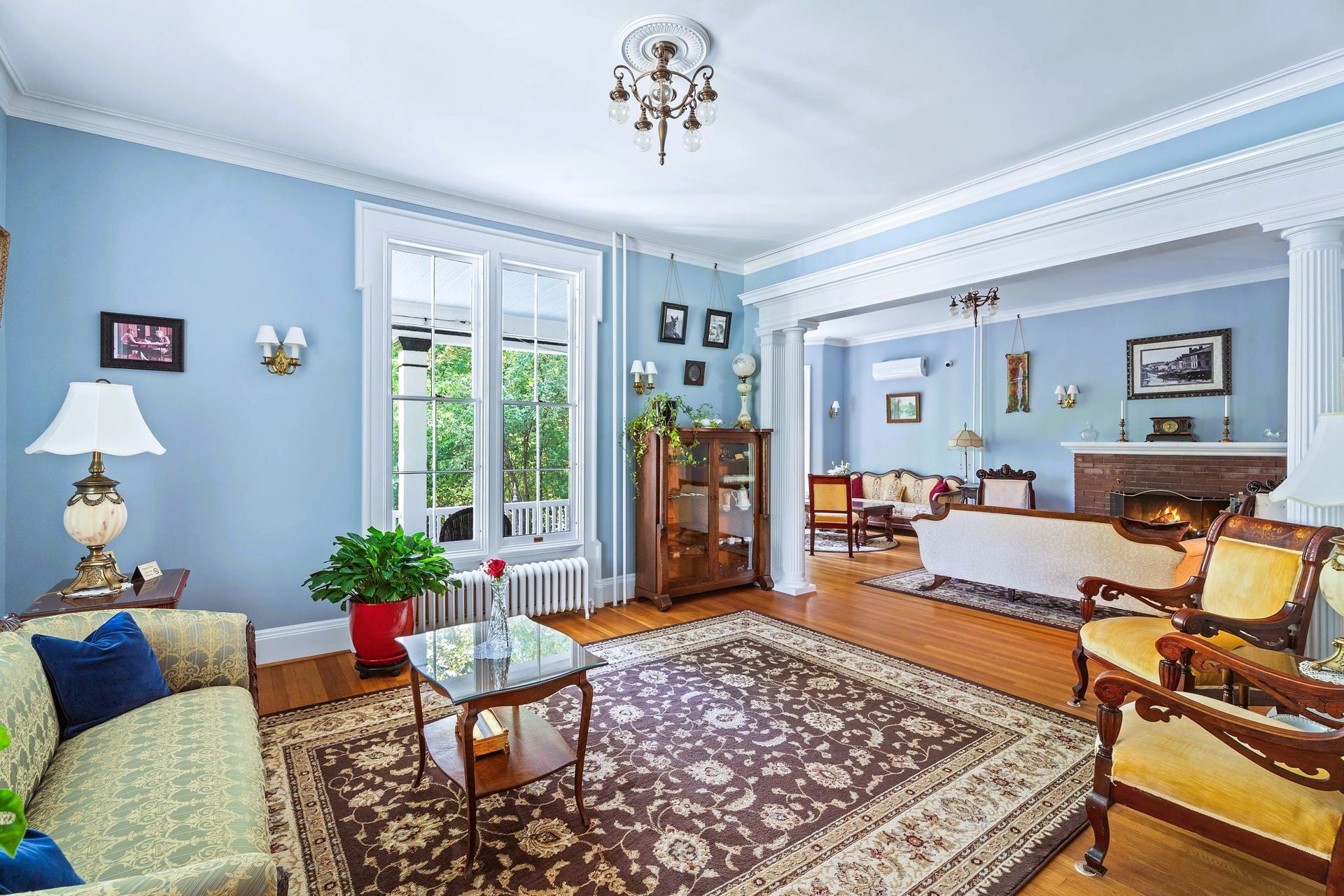 Bright blue living room with patterned rug, sofa, armchairs, fireplace, and tall windows.