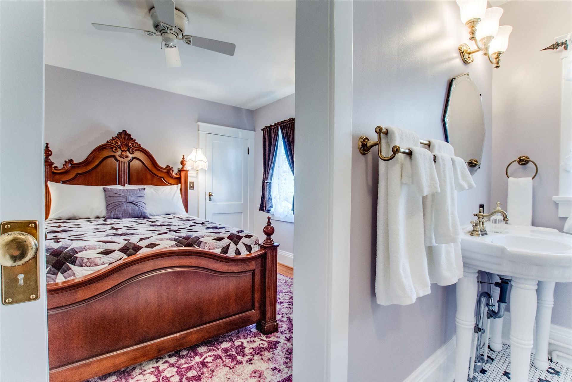 Bedroom and bathroom view with carved wooden bed, floral bedding, and white towels by pedestal sink