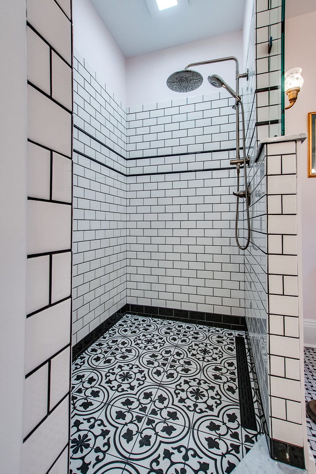 Small white tiled shower with patterned black-and-white floor and a handheld showerhead.