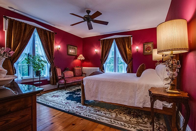 Elegant red bedroom with canopy bed, large windows, patterned rug, and warm bedside lamp lighting