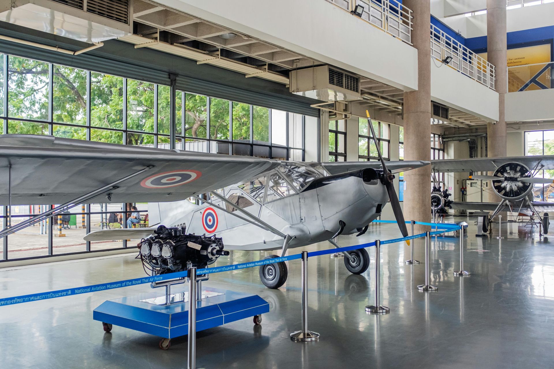Vintage gray airplane on display in a bright museum hall, roped off on stands.