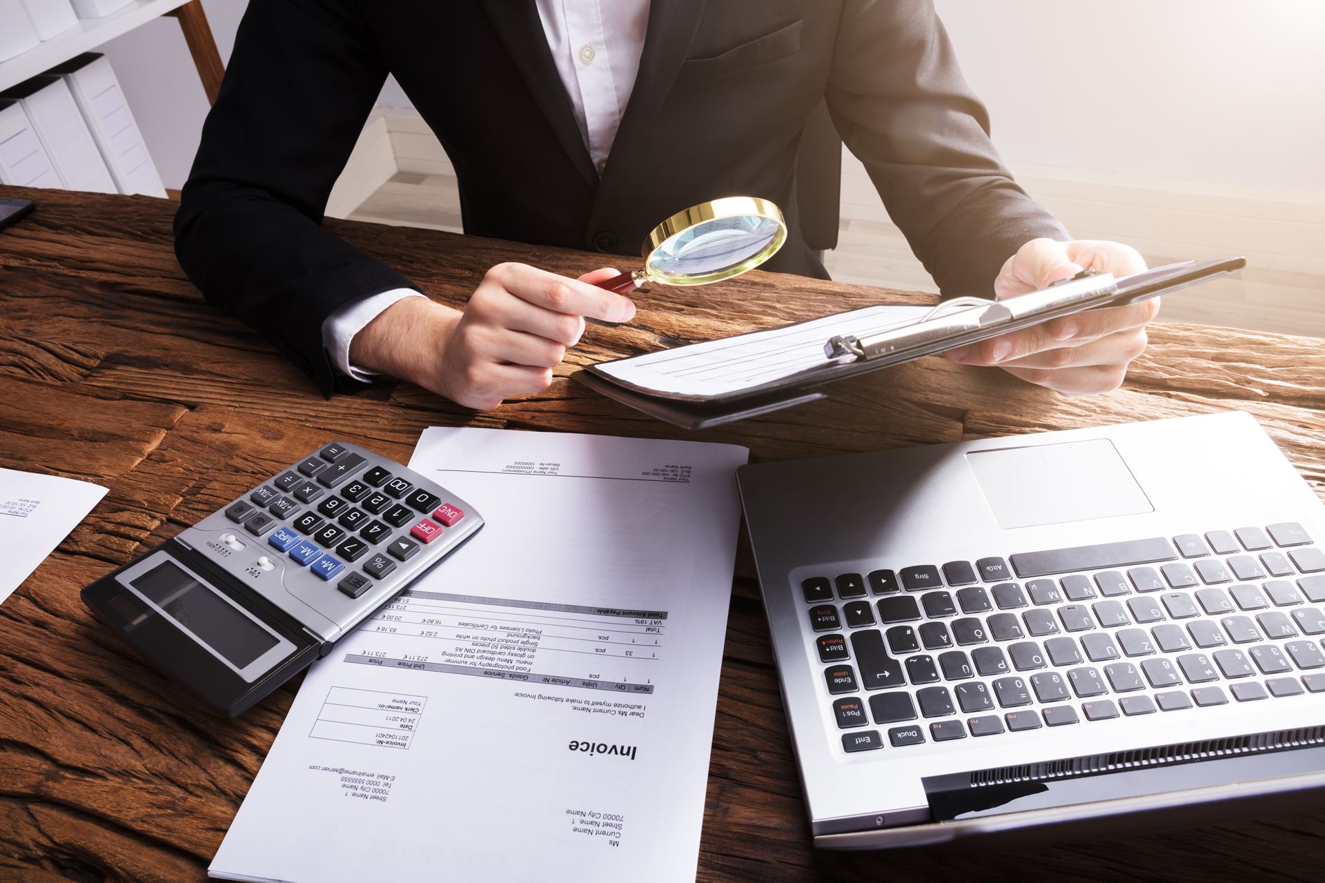 A man is sitting at a desk looking at a clipboard with a magnifying glass.