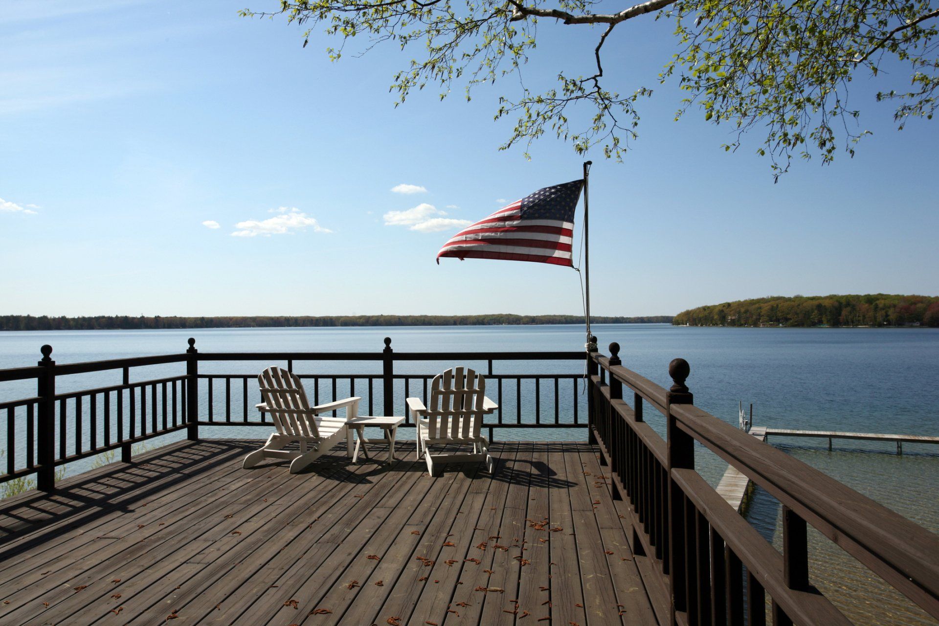 A deck with chairs and an american flag on it overlooking a lake