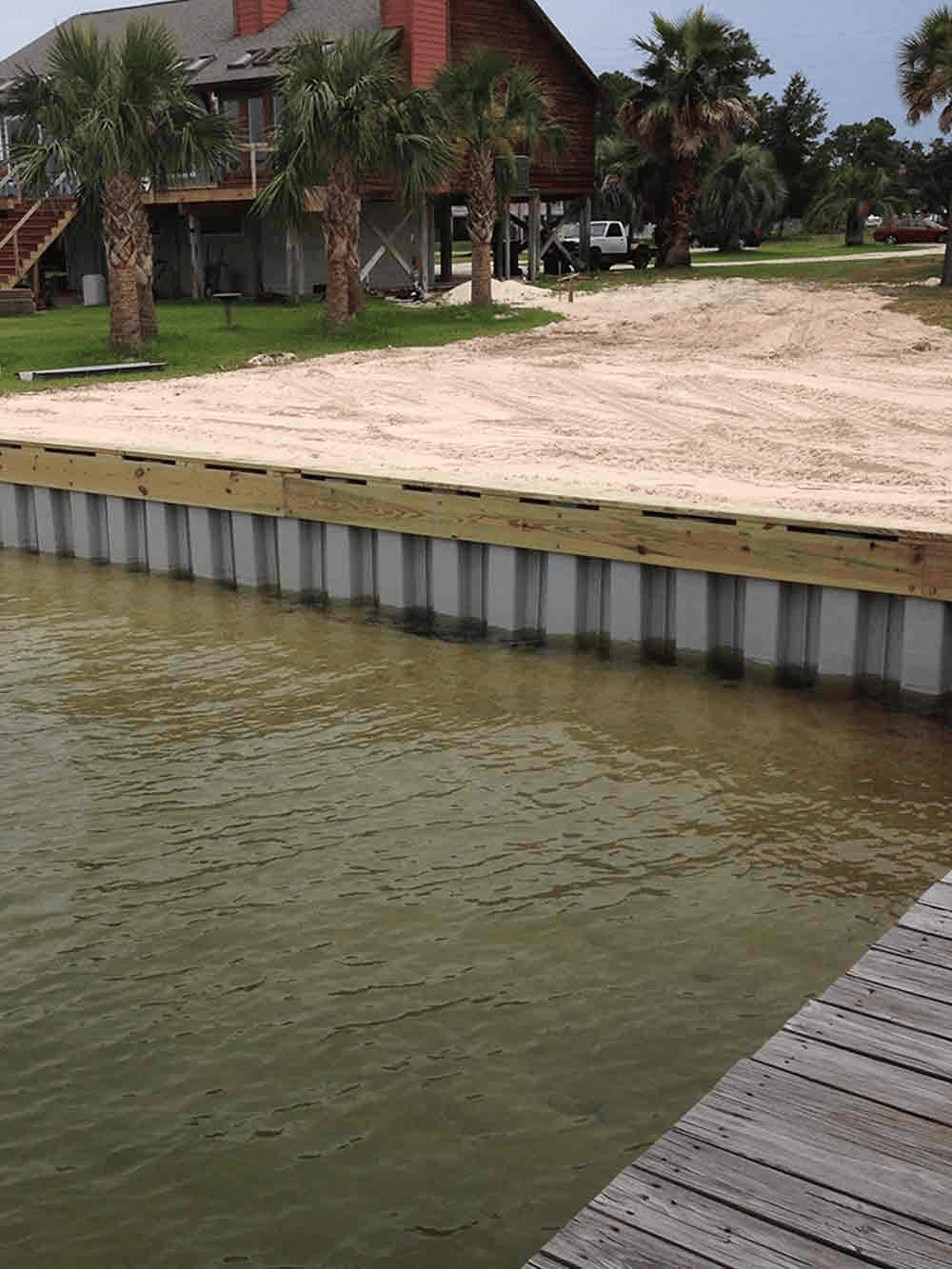 A wooden dock is next to a body of water with a house in the background.