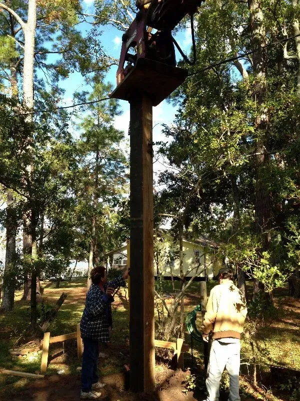 Two people are standing next to a wooden pole in the woods