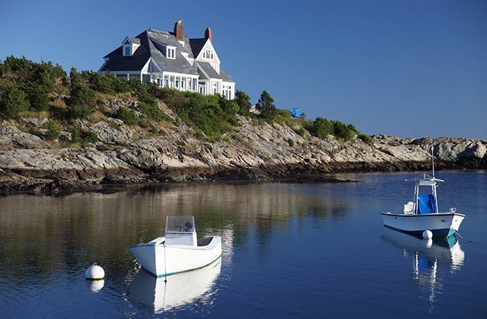 A house sits on top of a rocky hill overlooking a body of water.