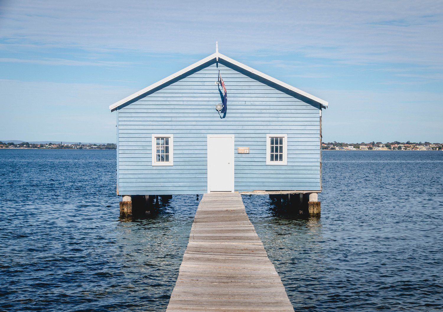 A small blue house is sitting on top of a wooden dock in the middle of the ocean.