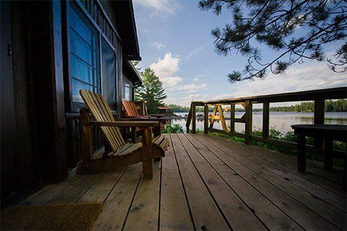 A wooden deck with chairs on it overlooking a lake.