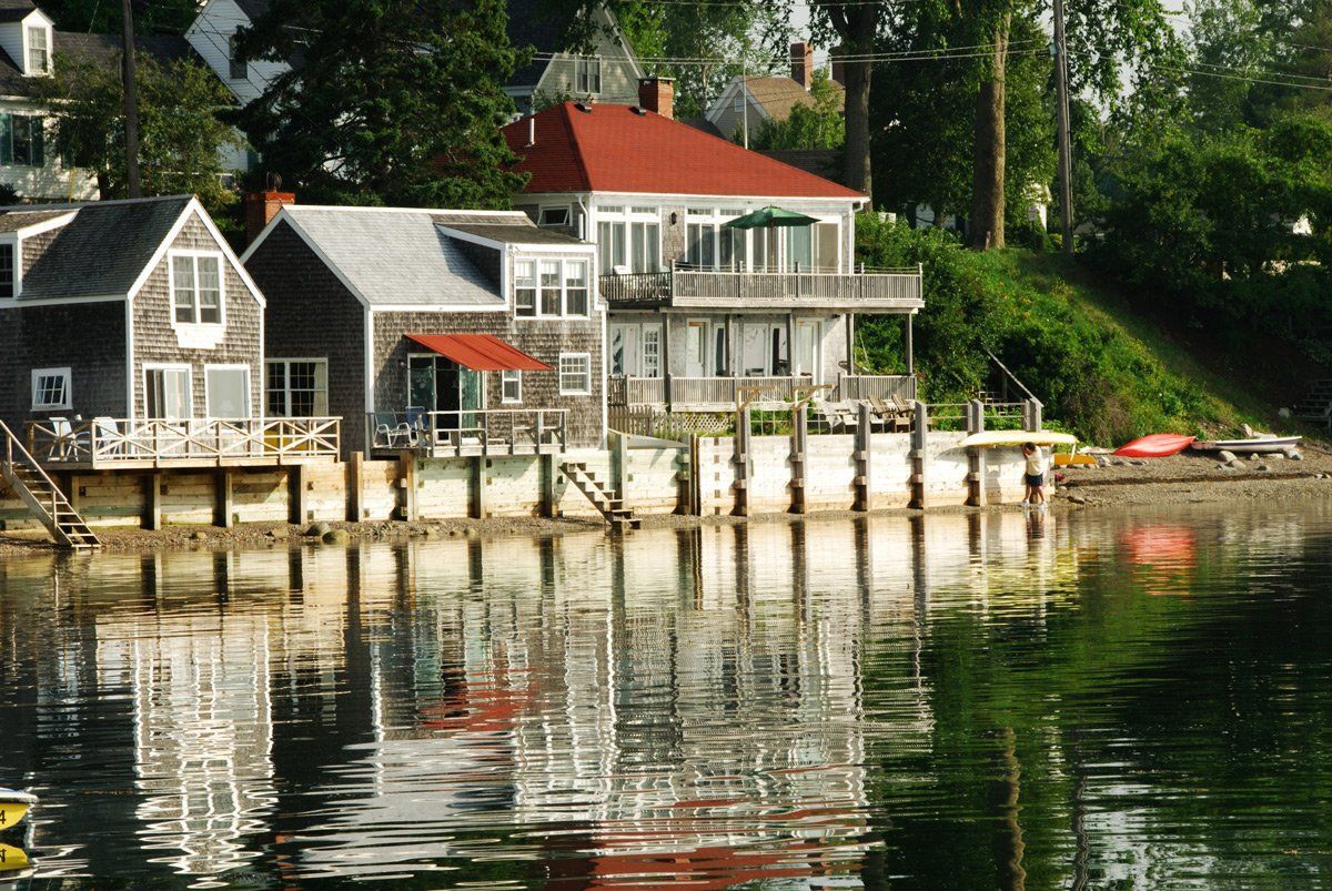 A house with a red roof sits next to a body of water