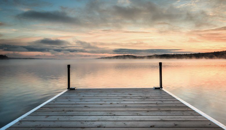 A wooden dock leading into a lake at sunset.