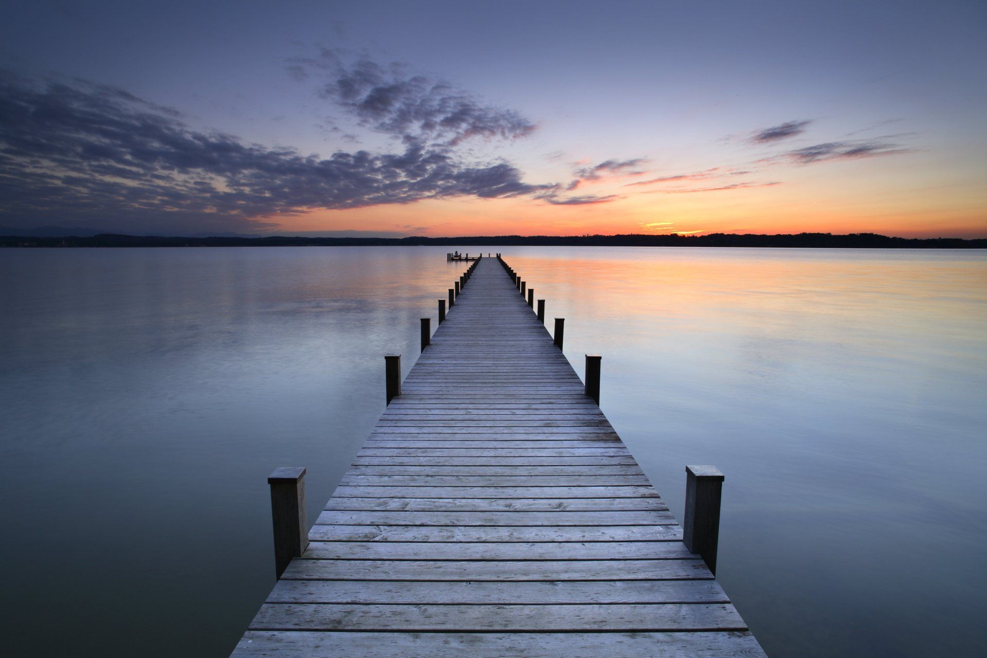 A long wooden dock leading into a body of water at sunset