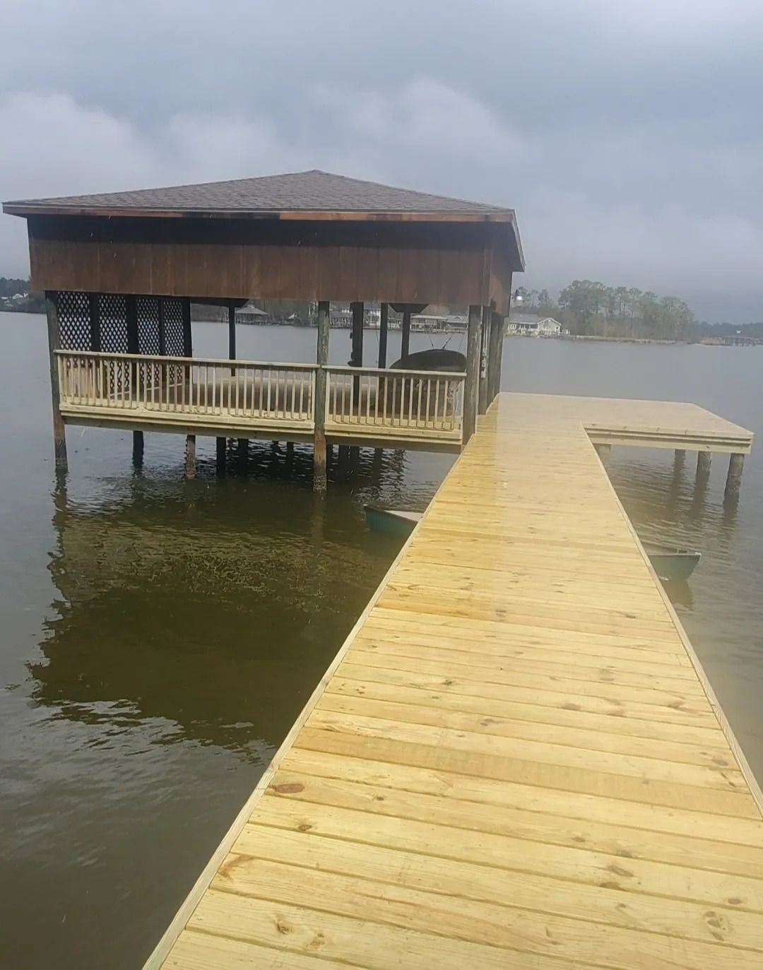 A wooden dock with a gazebo on top of it in the middle of a lake.